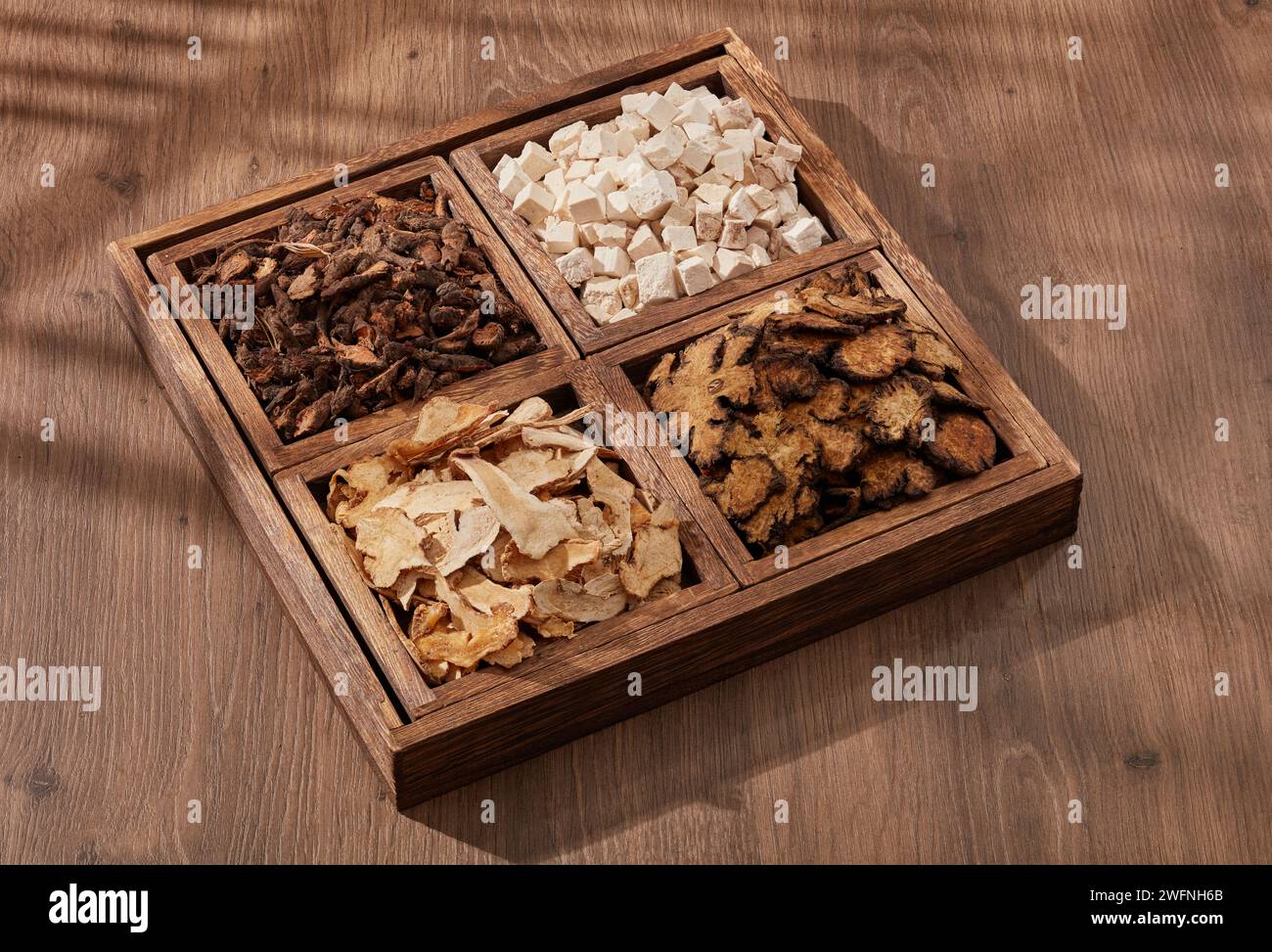 A square wooden tray with 4 compartments containing Poria cocos, Szechuan Lovage Rhizome and other herbs. Traditional chinese medicine concept Stock Photo