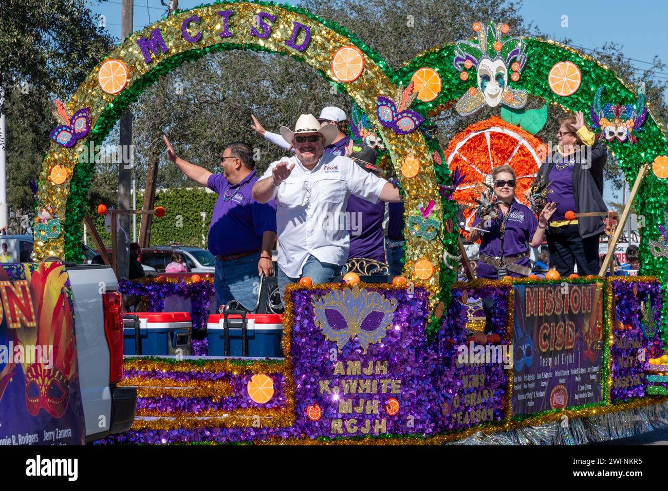 People wave from purple and green parade float for Mission School District in 92nd Annual Texas Citrus Fiesta Parade of Oranges, Mission, Texas, USA. Stock Photo