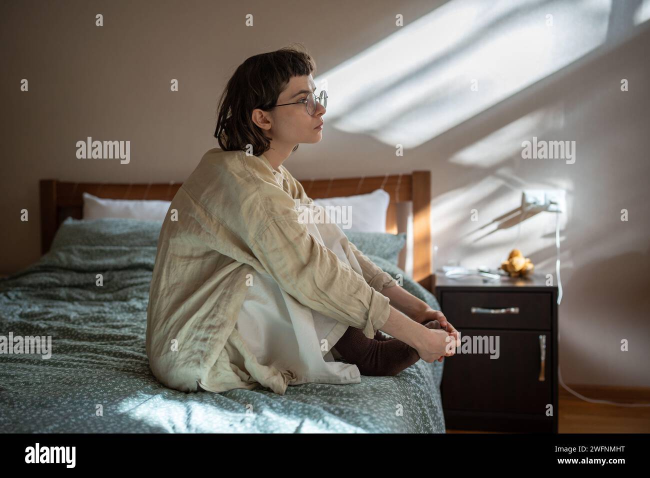 Melancholic teen girl sitting on bed in apathetical, depressed mood, thinking of misunderstanding Stock Photo