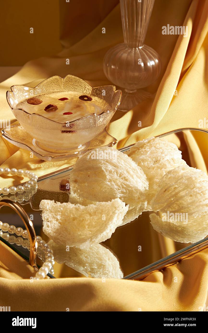 A glass bowl of bird nest soup with jujube and dried goji berries decorated with edible bird nest placed on a mirror tray. Elegant yellow fabric backg Stock Photo
