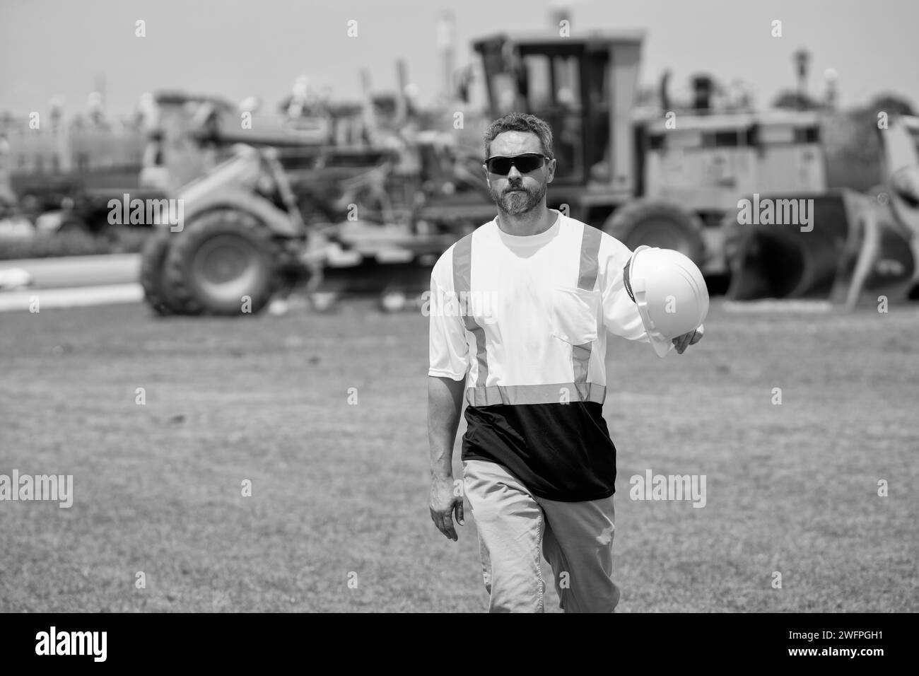 Mature architect walking in construction area. employee construction man in vest protective hardhat walking outdoor. Construction site with heavy Stock Photo