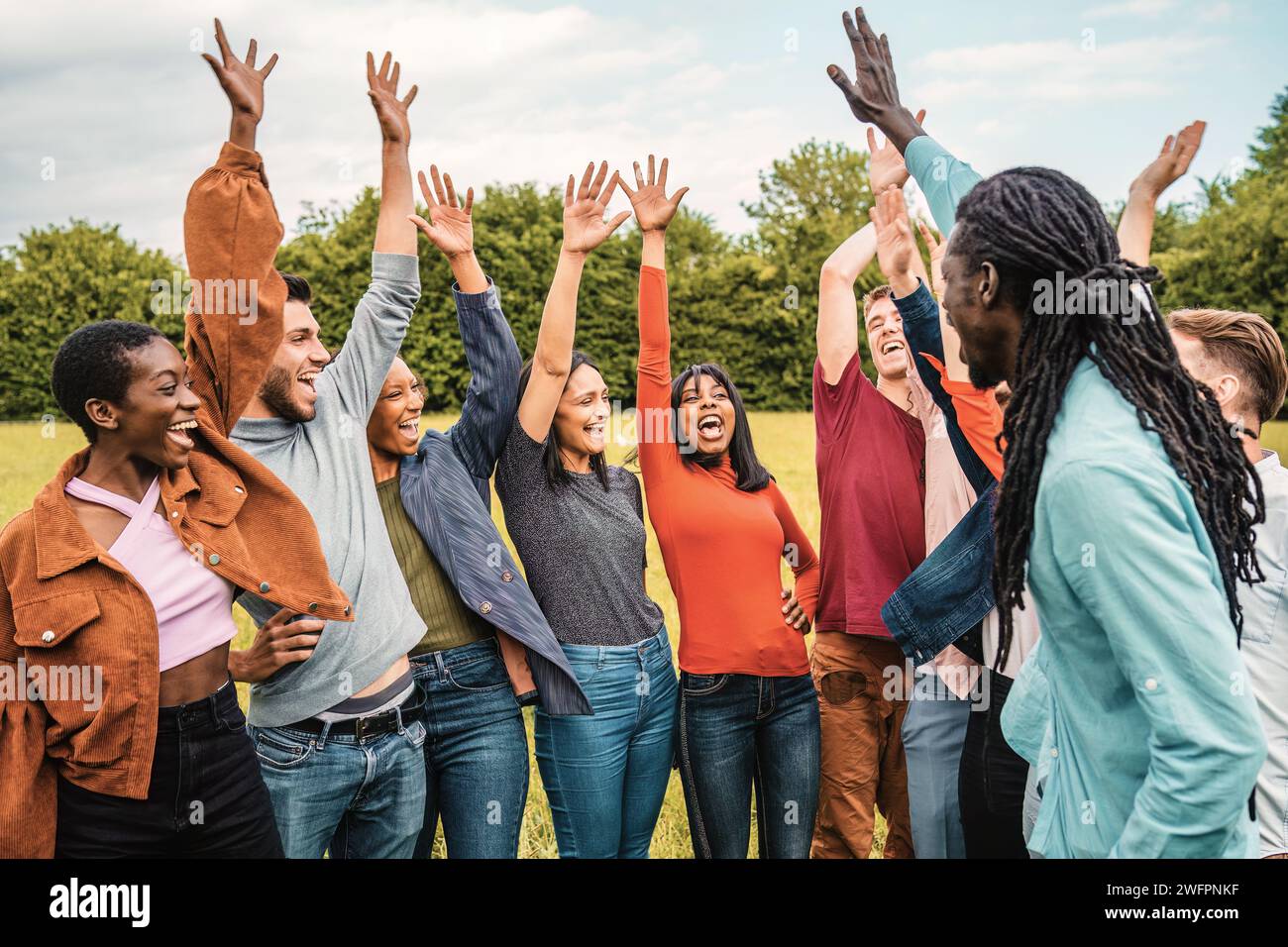 A vibrant group of friends cheerfully raise their hands in celebration, enjoying a lively moment in the park. Stock Photo