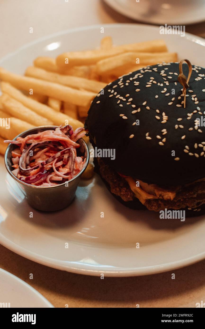 French fries and a beef burger with a black bun in a cafe. American delicious lunch Stock Photo