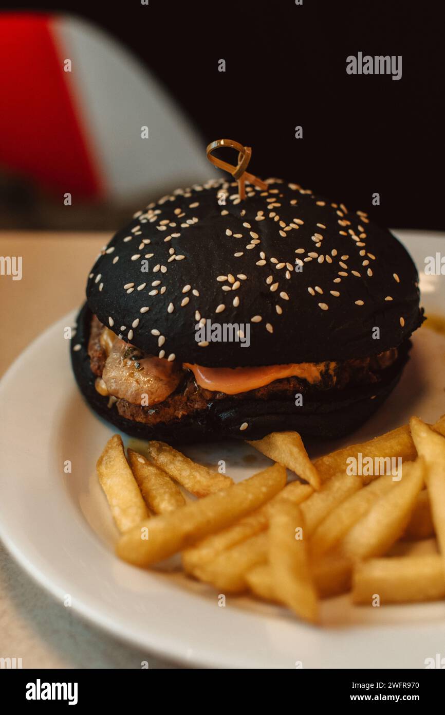 French fries and a beef burger with a black bun in a cafe. American delicious lunch Stock Photo