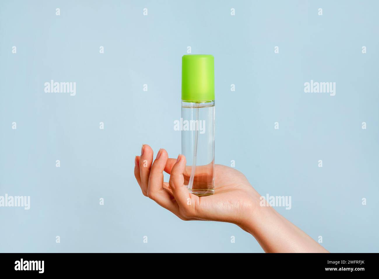 Perfume and toilet water. Woman's hand holds a glass perfume bottle, close-up. blue background with copy space Stock Photo