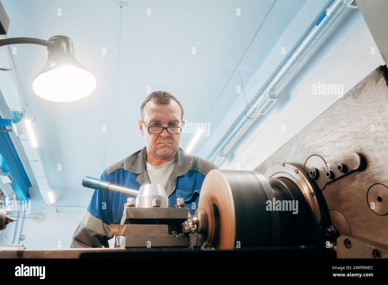 Elderly turner, 50-55 years old, works at lathe in turning shop. Front ...