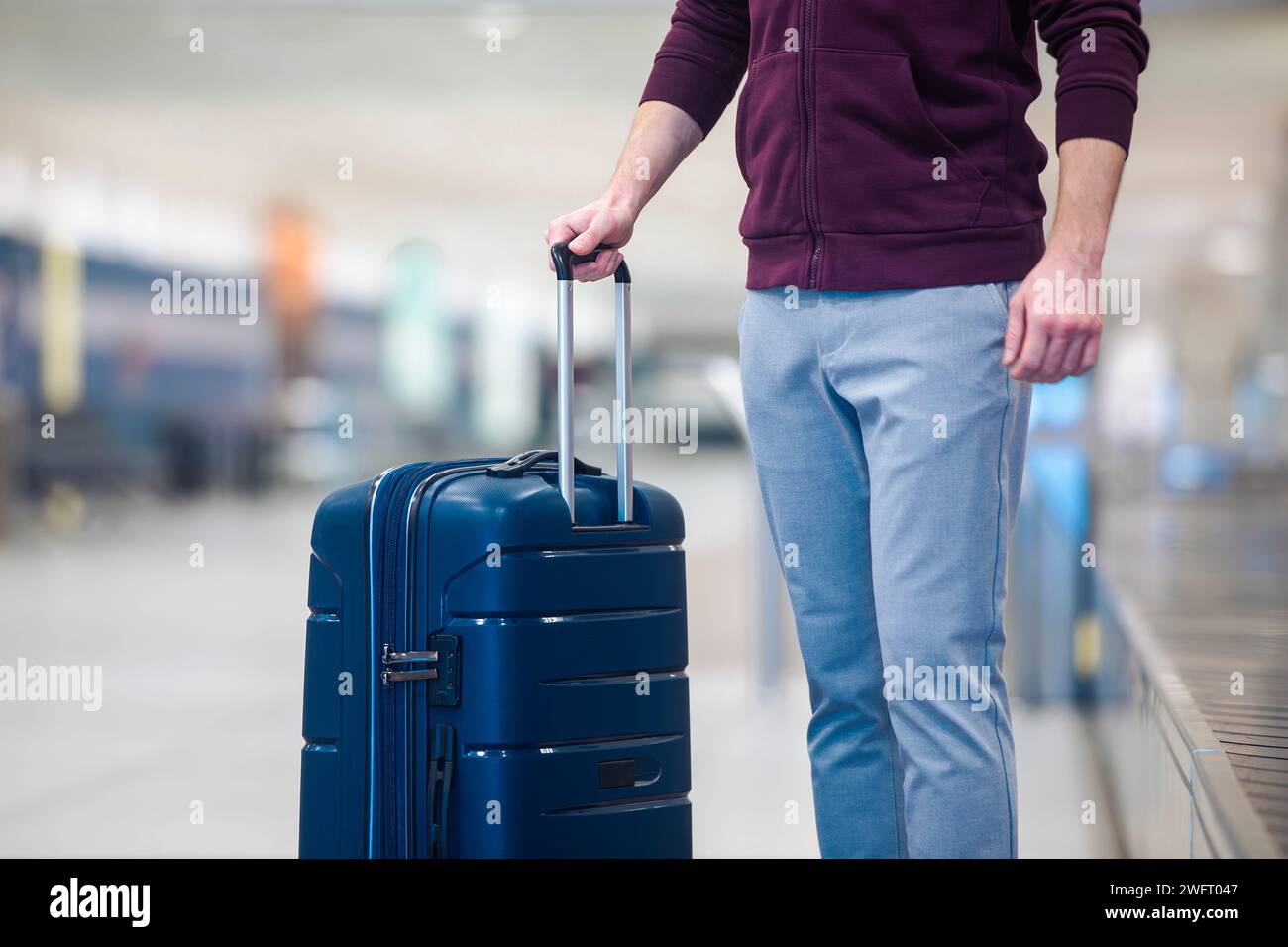 Passenger traveling by plane picking up blue suitcase from conveyor belt in airport arrivals terminal. Stock Photo