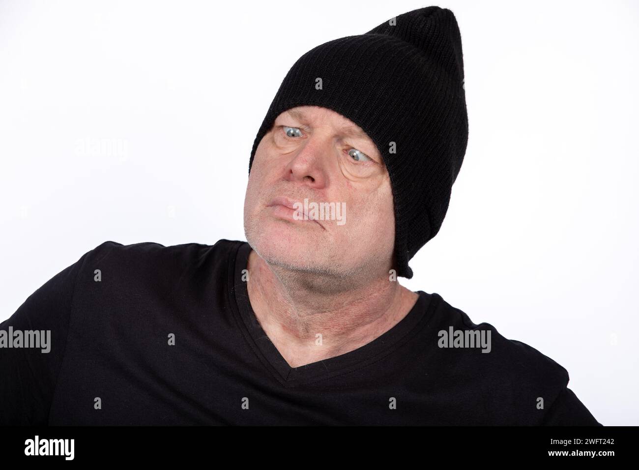 Quirky Middle-Aged Man in Black T-Shirt and Hat with Cross-Eyed Expression, Humorous Character on White Background - Eccentric Portrait Concept Stock Photo