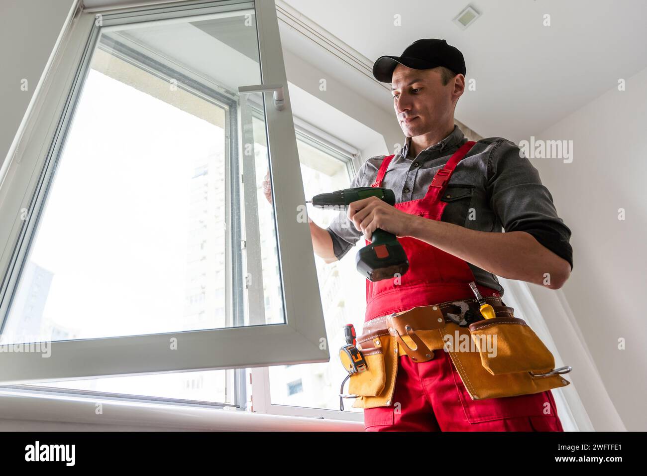 Professional installer of plastic windows poses in a working uniform, holds glasses with his hand. Specialist in the installation of plastic windows Stock Photo