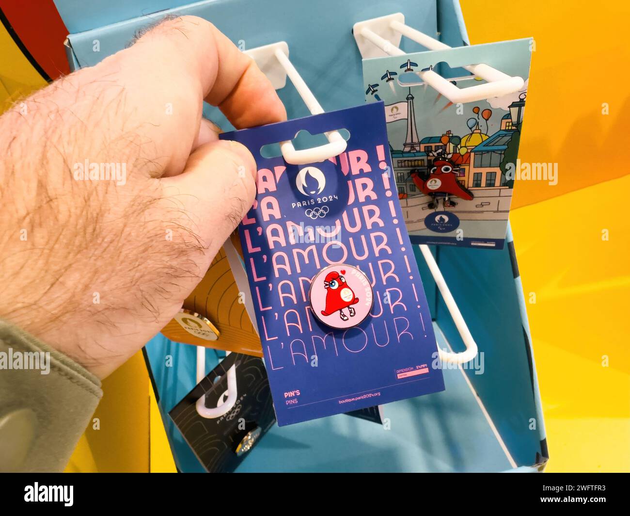 Hand holding 2024 Paris Olympic Phryges Caps pin, purchased in a dedicated fan shop zone