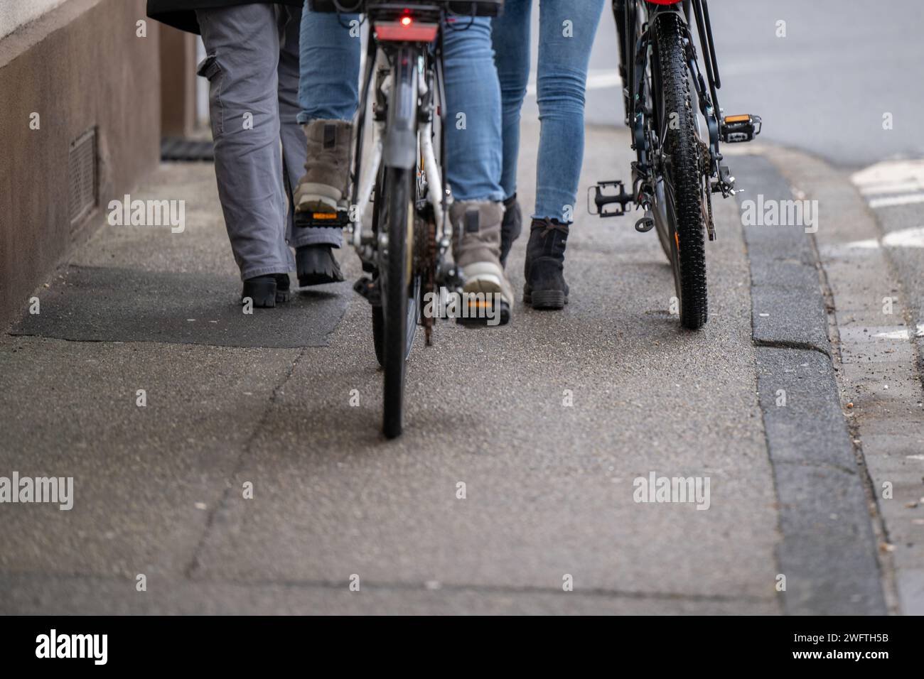 , Alltagssituation, Deutschland, 01.02.2024,  Zwei Personen gehen auf einem Gehweg, eine davon schiebt ein Fahrrad mit einem Korb und einem Helm auf d Stock Photo