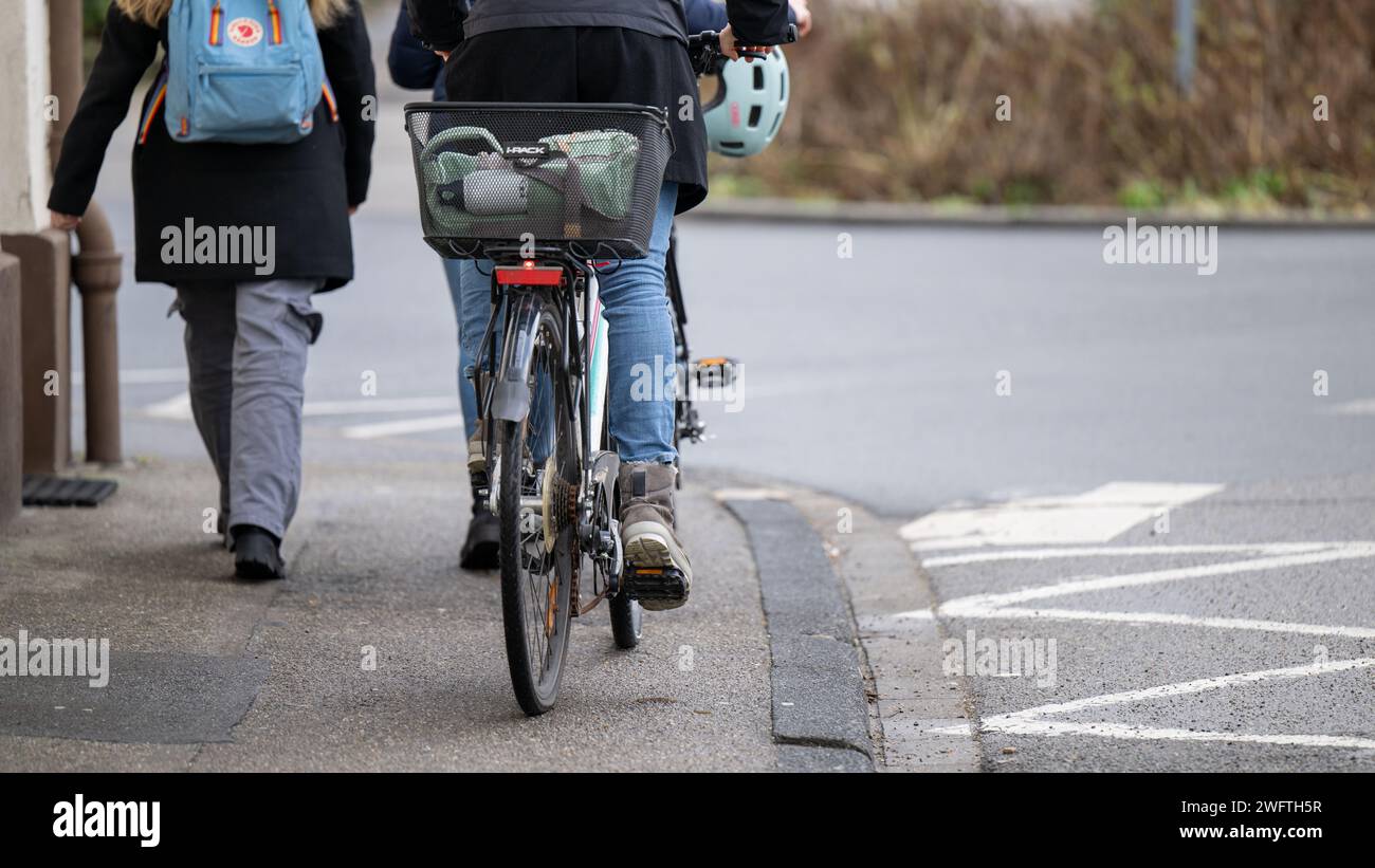 , Alltagssituation, Deutschland, 01.02.2024,  Zwei Personen gehen auf einem Gehweg, eine davon schiebt ein Fahrrad mit einem Korb und einem Helm auf d Stock Photo