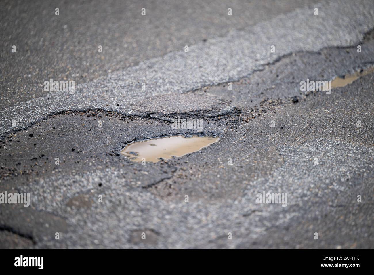 Asphaltstraße mit Schlagloch und Rissen , Alltag, 01.02.2024, Detailaufnahme eines Schlaglochs in einer asphaltierten Straße, umgeben von Rissen und beschädigtem Belag. Die Textur des Asphalts und das stehende Wasser im Schlagloch sind deutlich sichtbar. *** Asphalt road with pothole and cracks , Everyday life, 01 02 2024, Close-up of a pothole in an asphalt road, surrounded by cracks and damaged pavement The texture of the asphalt and the standing water in the pothole are clearly visible Stock Photo