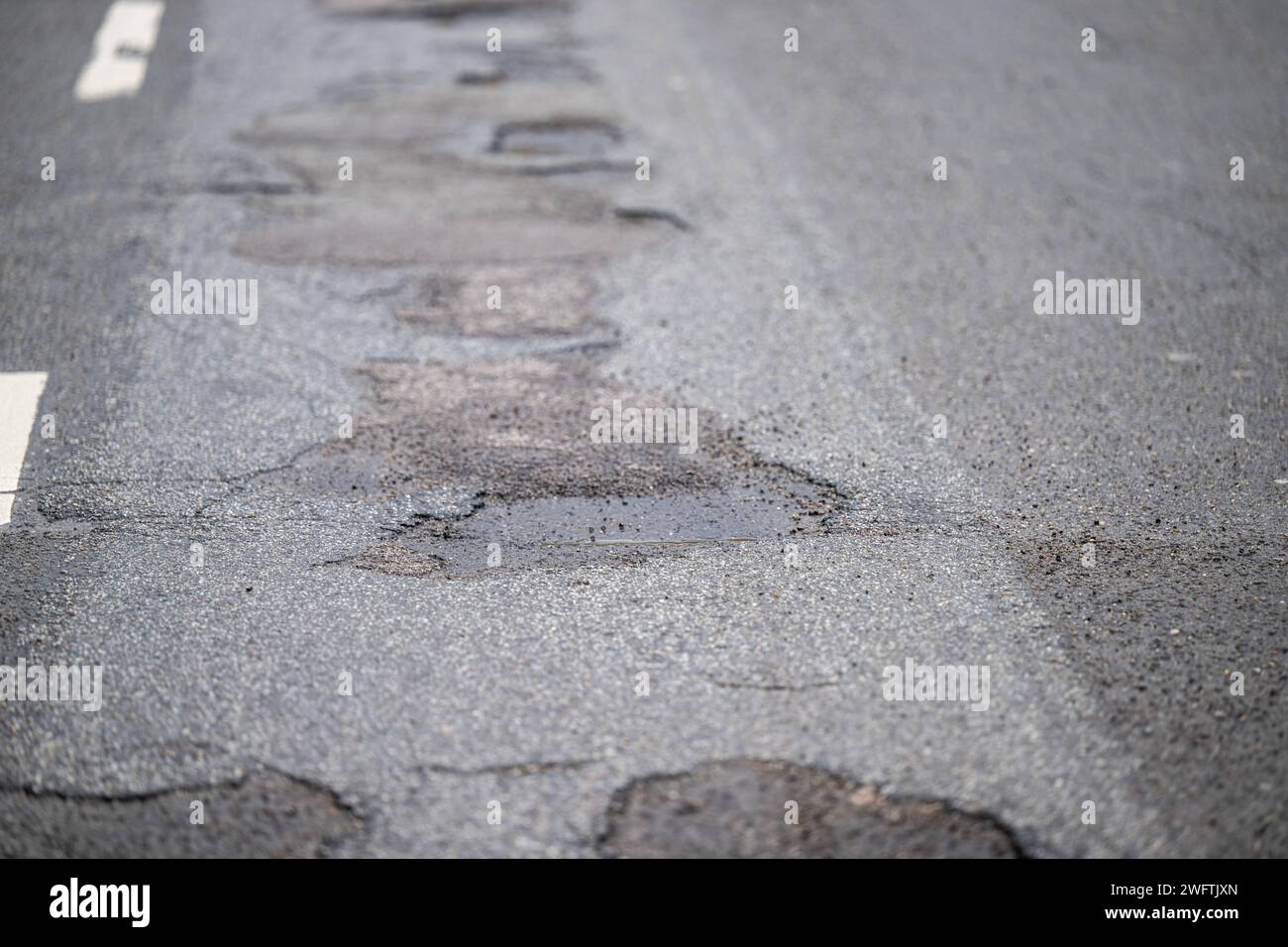 Asphaltstraße mit Schlagloch und Rissen , Alltag, 01.02.2024, Detailaufnahme eines Schlaglochs in einer asphaltierten Straße, umgeben von Rissen und beschädigtem Belag. Die Textur des Asphalts und das stehende Wasser im Schlagloch sind deutlich sichtbar. *** Asphalt road with pothole and cracks , Everyday life, 01 02 2024, Close-up of a pothole in an asphalt road, surrounded by cracks and damaged pavement The texture of the asphalt and the standing water in the pothole are clearly visible Stock Photo