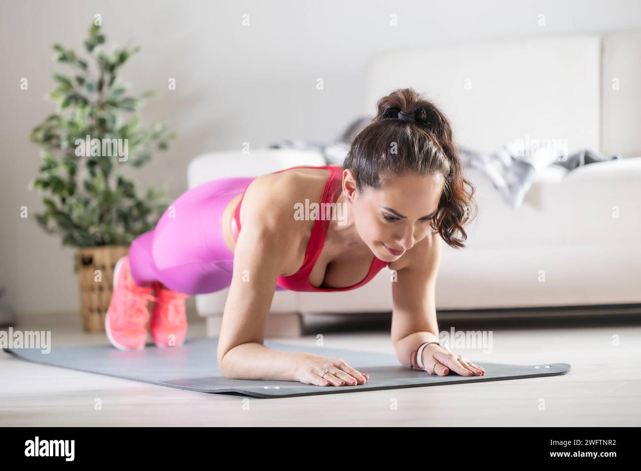 A beautiful fitness woman in sportswear is doing plank exercises. He trains at home in his living room on a mat. Stock Photo