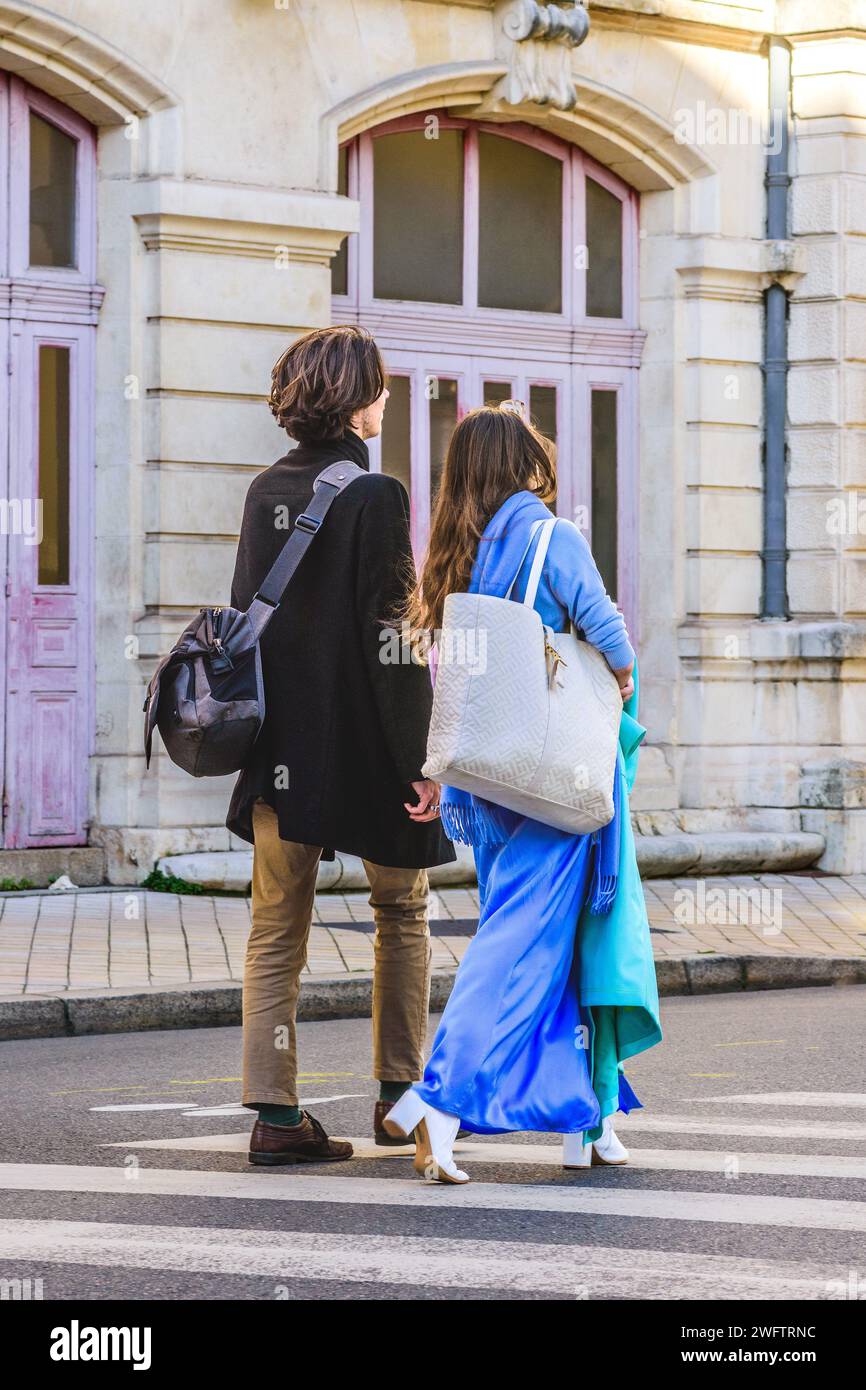 Rear view of smart couple - woman in sky blue coat - walking across city street - Tours, Indre-et-Loire (37), France. Stock Photo