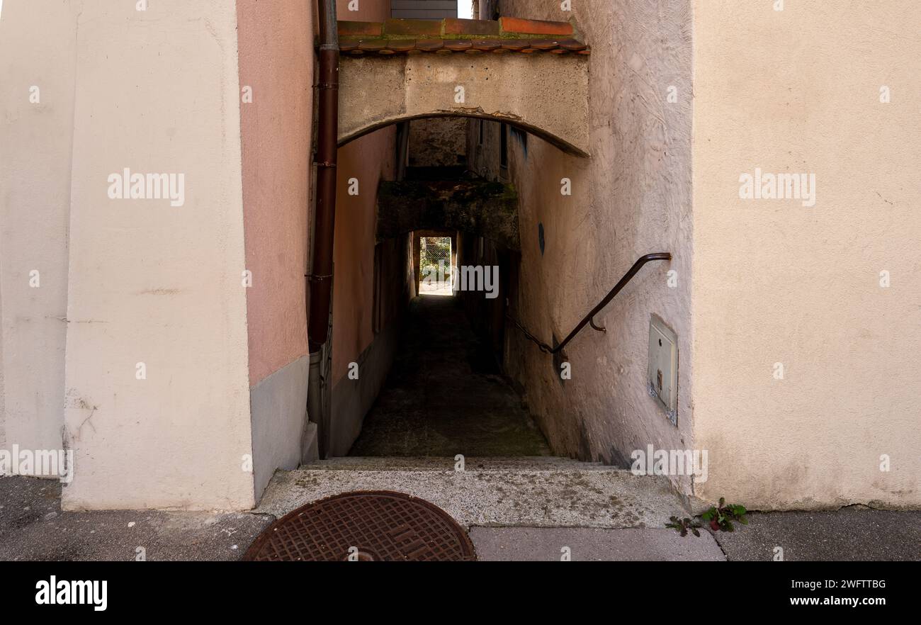 Old and dark passage between two houses in Aarau. Stairs with metal handrail leading down. Exist can be seen in the distance. Stock Photo