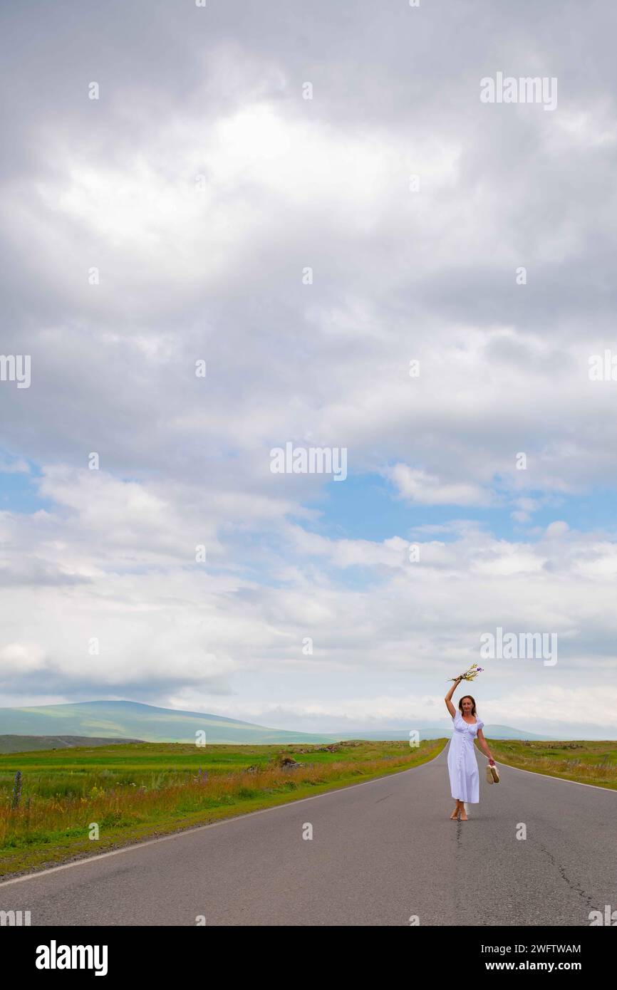 A girl in a white dress is walking with flowers on the road Stock Photo ...