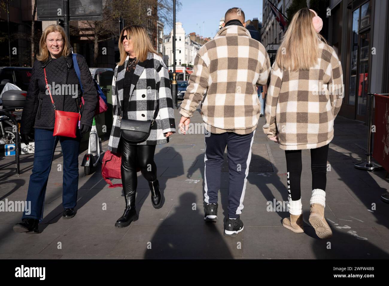 A couple holding hands walk through the West End wearing identical chequered coats, on 1st February 2024, in London, England. Stock Photo