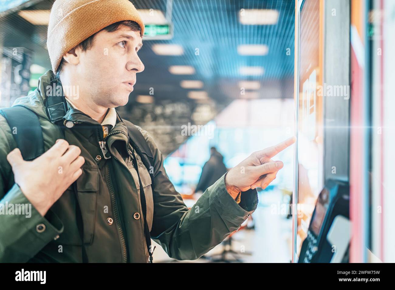 Young man using self-service terminal with big sensor screen to buy ...