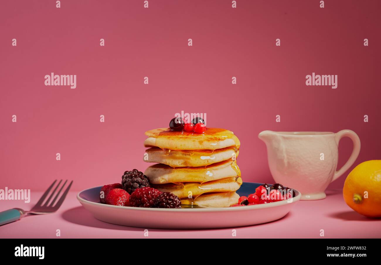 Stack of pancakes with mixed berries and garnished with honey shot on a pink background. Stock Photo