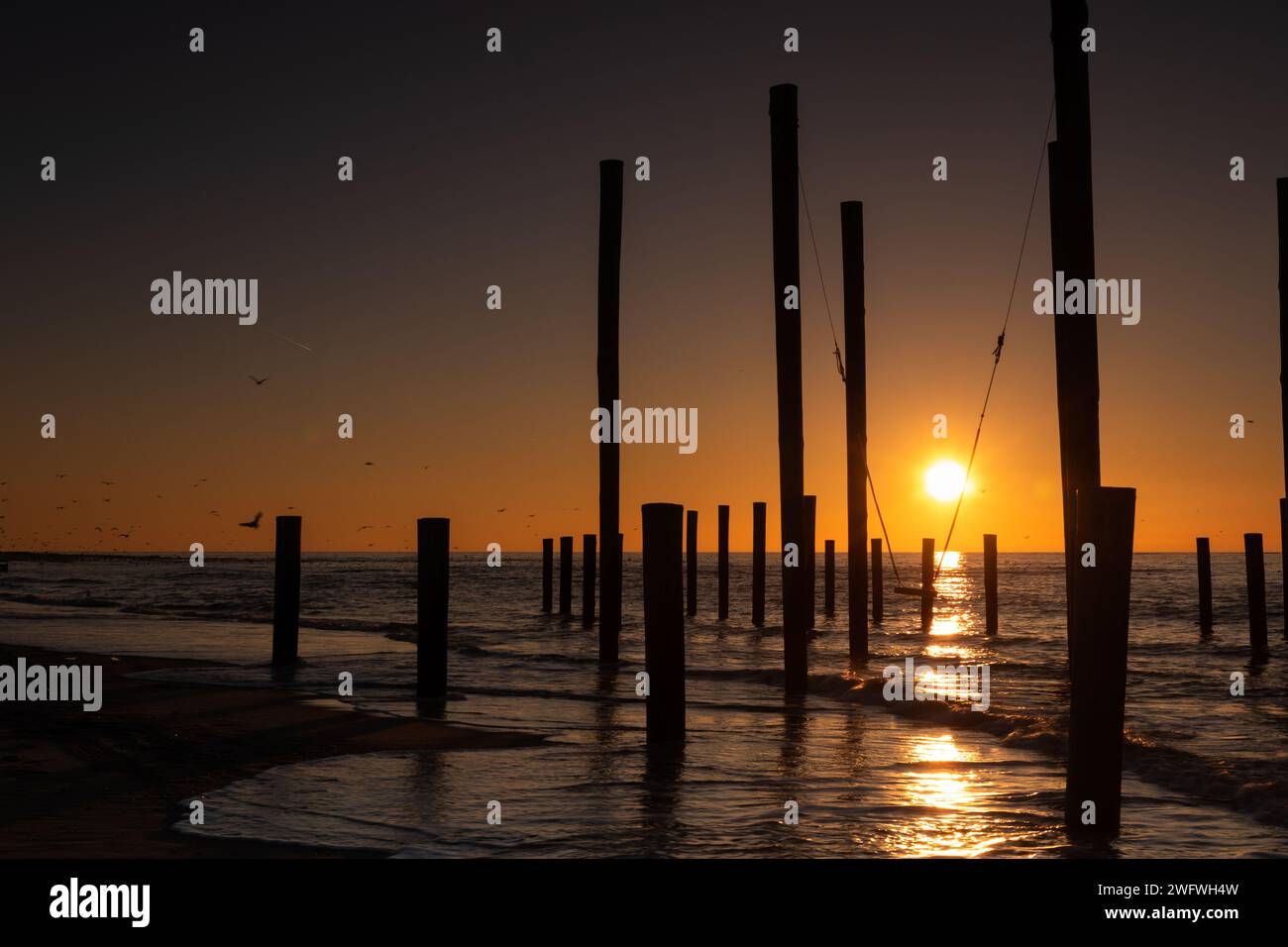 Monumental wooden poles, including a swing set, in the sea during a lovely sunset in the Netherlands Stock Photo