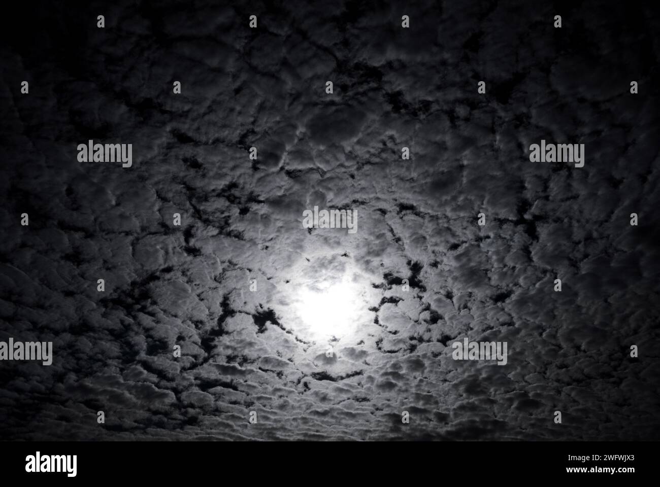 the sun hidden behind altocumulus clouds Stock Photo