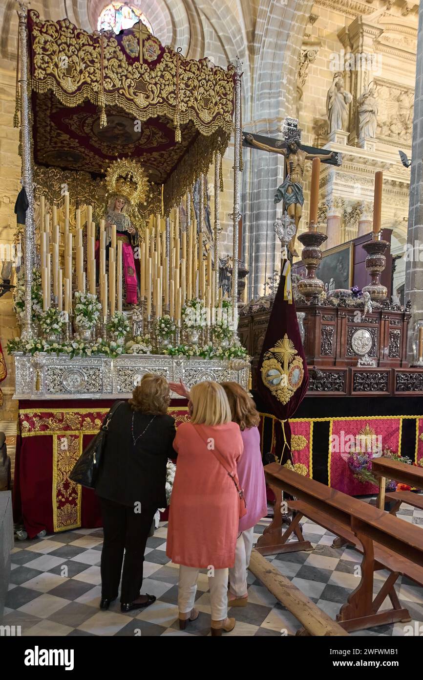 Jerez de la Frontera, Spain - February 01, 2024: Three women look at a church altar adorned with gold details, flowers and religious icons in Jerez de Stock Photo