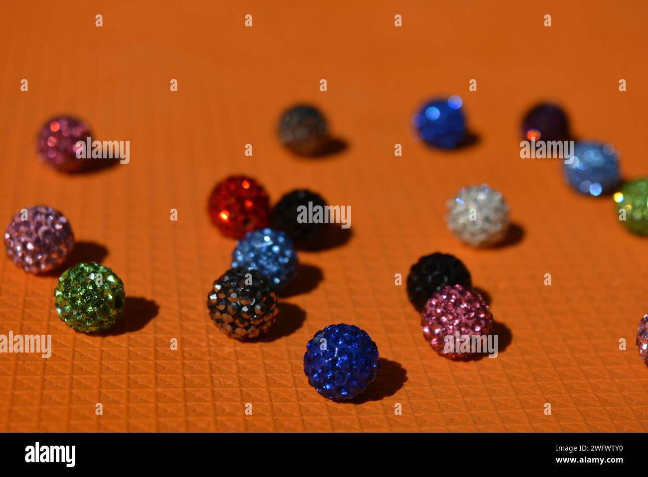 Beautiful, bright, multi-colored balls with Swarovski crystals chaotically arranged on a bright orange background. Stock Photo