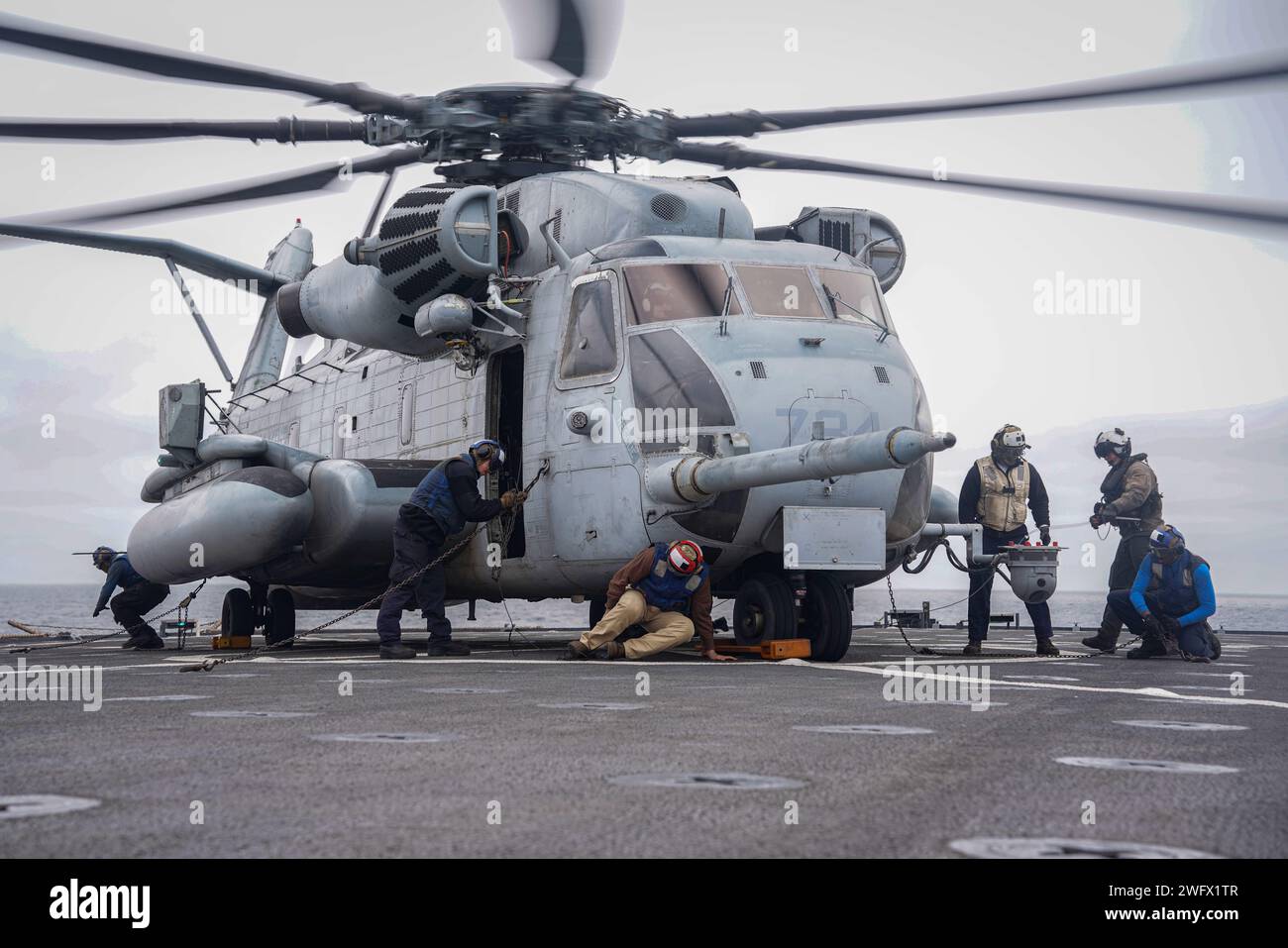 Sailors use chocks and chains to secure a CH-53E Super Stallion, attached to Marine Medium Tilt-rotor Squadron (VMM) 165, 15th Marine Expeditionary Unit (MEU), aboard the amphibious dock landing ship USS Harpers Ferry (LSD 4), during flight quarters while underway in the Pacific Ocean, Jan. 15, 2024. The Boxer Amphibious Ready Group, comprised of USS Boxer (LHD 4), USS Somerset (LPD 25), and Harpers Ferry, and the embarked 15th Marine Expeditionary Unit are underway conducting integrated training and routine operations in U.S. 3rd Fleet. Stock Photo
