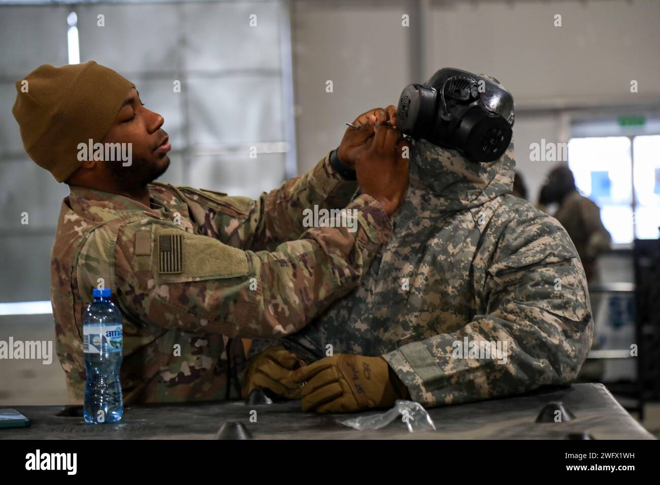 U.S. Army Sgt. Christian Robinson, a chemical, biological, radiological and nuclear specialist assigned to the 87th Division Sustainment Support Battalion, 3rd Division Sustainment Brigade, known as Task Force Provider, assists a Soldier donning protective clothing during a chemical attack drill at Karliki, Poland, Jan. 19, 2024. The 87th DSSB organized the training event to ensure Soldiers are ready to rapidly respond to protect themselves and continue operations even in chemical, biological, radiological and nuclear  environments. These Soldiers are deployed to Europe to assure allies and su Stock Photo