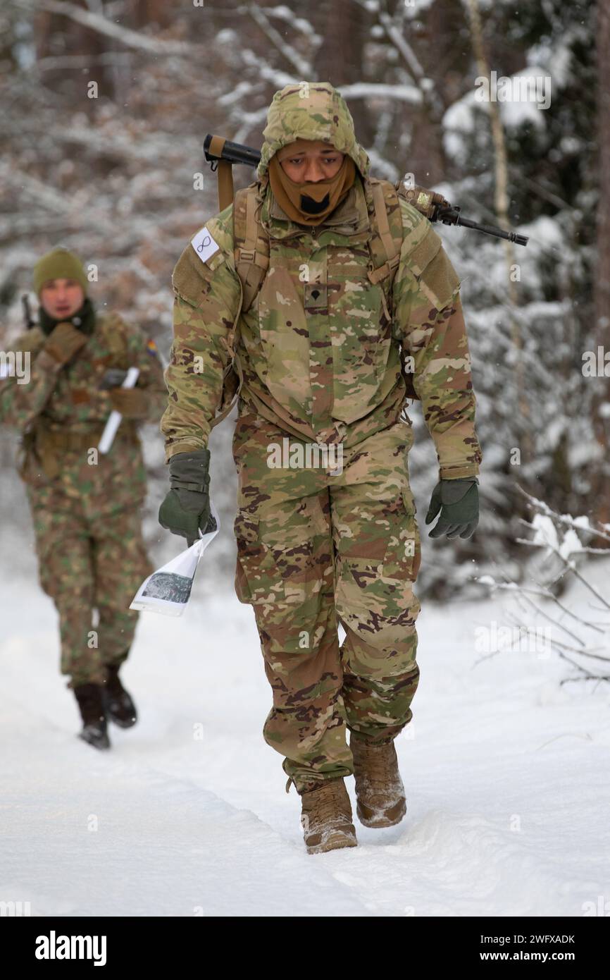 U.S. Army Spc. Kory Hubbard, with Headquarters and Headquarters “Hazard” Company, 2nd Battalion, 69th Armored Regiment “Panther Battalion,” 2nd Armored Brigade Combat Team, 3rd Infantry Division, walks down a snowy path in front of a Romanian Soldier during the Croatian “Winter Challenge” at Bemowo Piskie Training Area, Poland, Jan. 5, 2024. The Croatian “Winter Challenge” is a 15-kilometer competition consisting of seven events: land navigation, small arms firing, wall climbing, obstacle course while wearing a gas mask, rope crossing, low-crawl and obstacle climbing, and a hand grenade toss. Stock Photo
