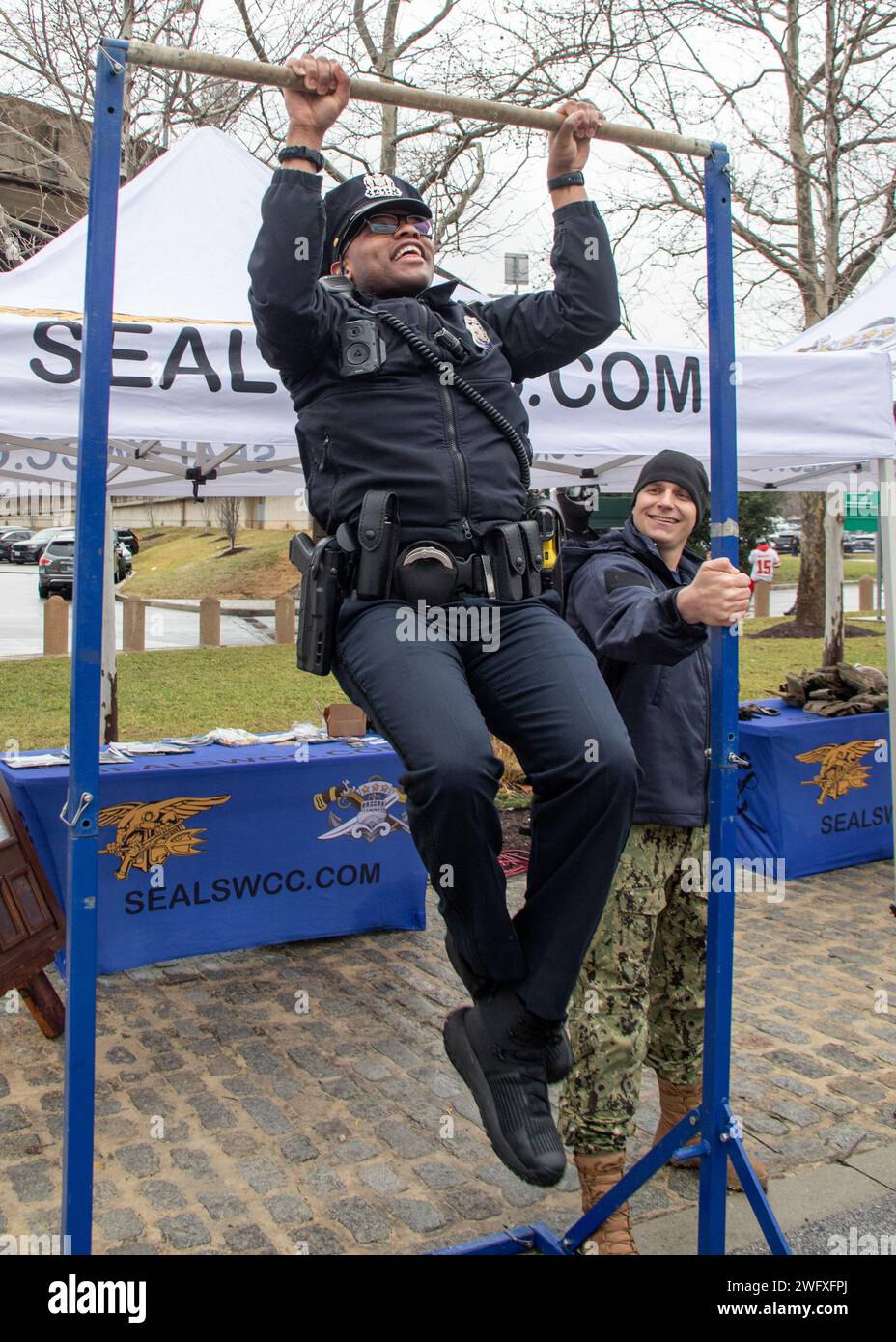 240128-N-LW994-1479 BALTIMORE (Jan. 28, 2024) A Baltimore City Police Officer makes his attempt of the pull-ups challenge during an outreach event at the NFL American Football Conference Championship game in Baltimore, Maryland. Naval Special Warfare is the nation's elite maritime special operations force, uniquely positioned to extend the Fleet's reach and gain and maintain access for the Joint Force in competition and conflict. Stock Photo