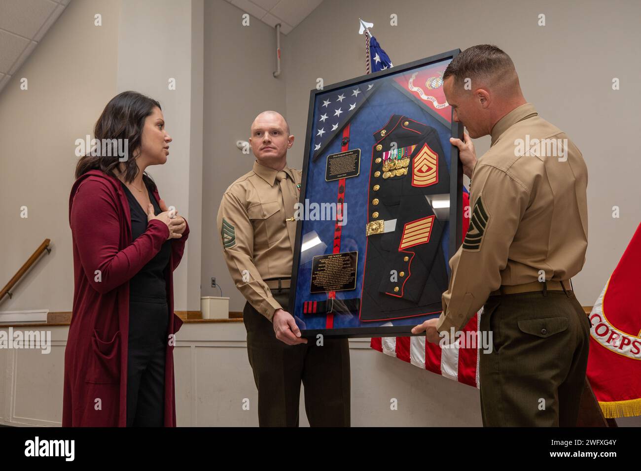 Josie Sevelius, left, and U.S. Marine Corps Gunnery Sgt. William M. Moore, center, the acting first sergeant of Logistics Operations Schools, present a gift to 1st Sgt. Neill A. Sevelius, right, following a retirement ceremony at Camp Gilbert H. Johnson, North Carolina, Jan. 11, 2024. The ceremony was held to recognize Sevelius’ 20 years of honorable service. Stock Photo