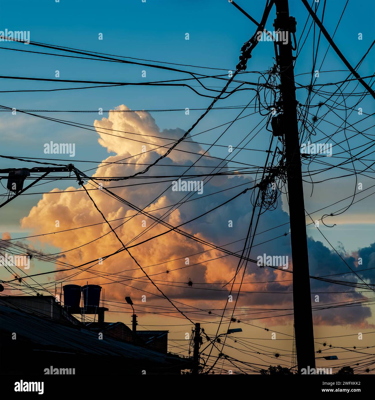 A beautiful large cloud imprisoned by the meshes of a tangle of electrical cables at sunset. Armenia, Quindío, Colombia. Stock Photo