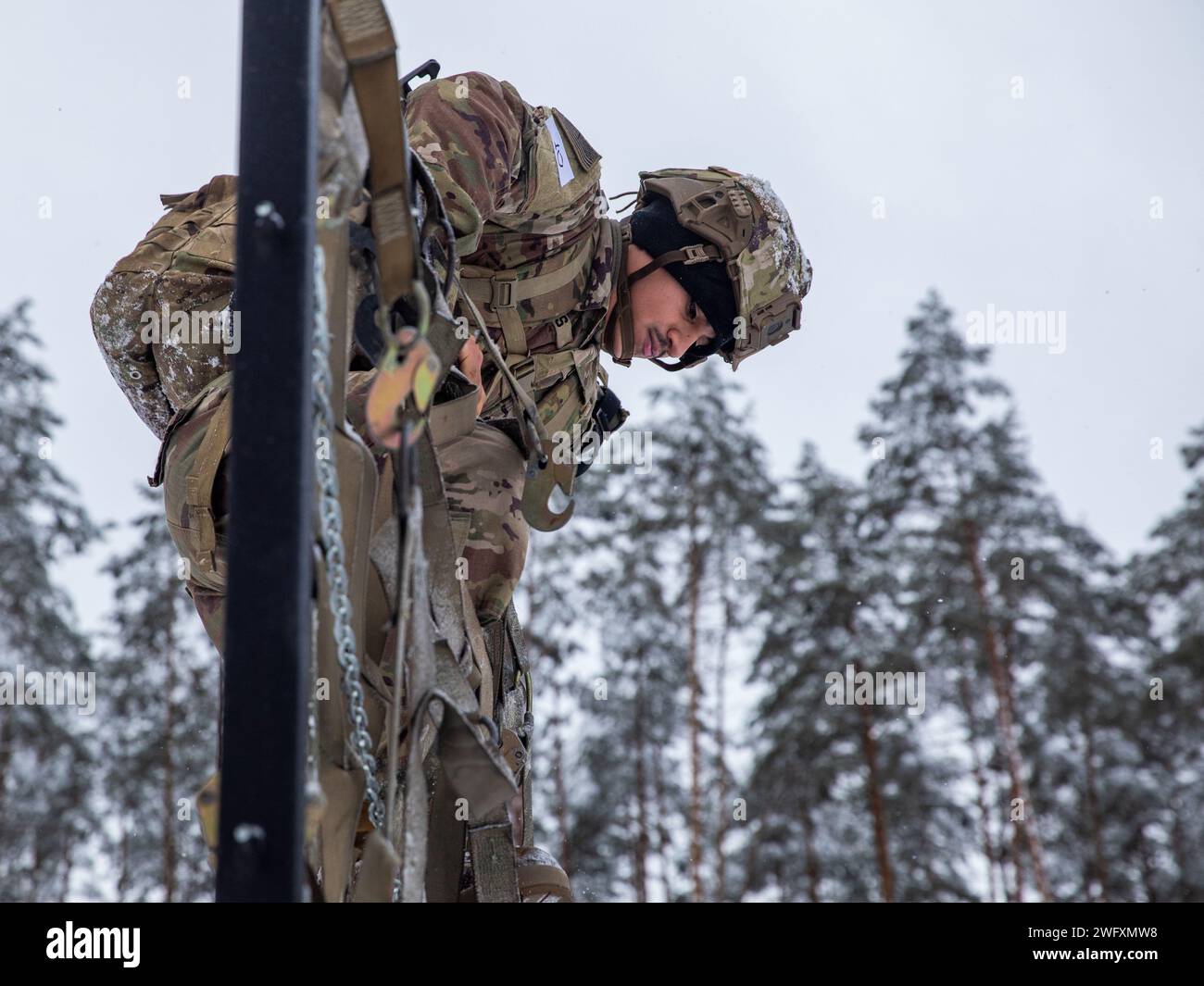 U.S. Army Spc. Jacob Serpas, an indirect fire infantryman with Headquarters and Headquarters “Hazard” Company, 2nd Battalion, 69th Armored Regiment “Panther Battalion,” 2nd Armored Brigade Combat Team, 3rd Infantry Division, climbs over an obstacle during the Croatian “Winter Challenge” at Bemowo Piskie Training Area, Poland, Jan. 5, 2024. The Croatian “Winter Challenge” is a 15-kilometer competition consisting of seven events: land navigation, small arms firing, wall climbing, obstacle course while wearing a gas mask, rope crossing, low-crawl and obstacle climbing, and a hand grenade toss. U. Stock Photo