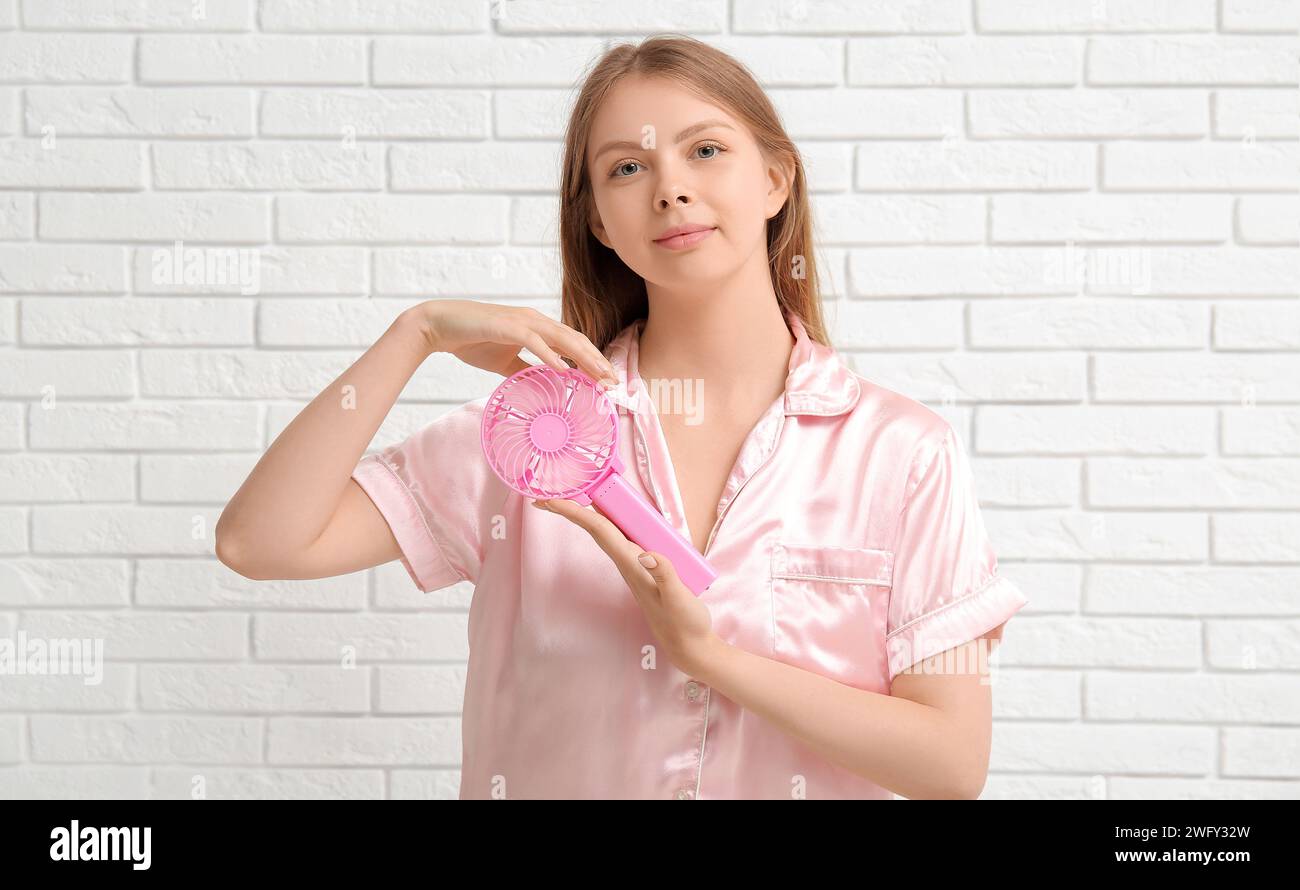 Beautiful young woman with handheld mini fan on white brick background ...