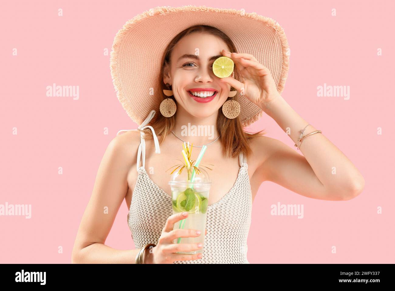 Beautiful young woman in wicker hat with glass of tasty mojito on pink background Stock Photo