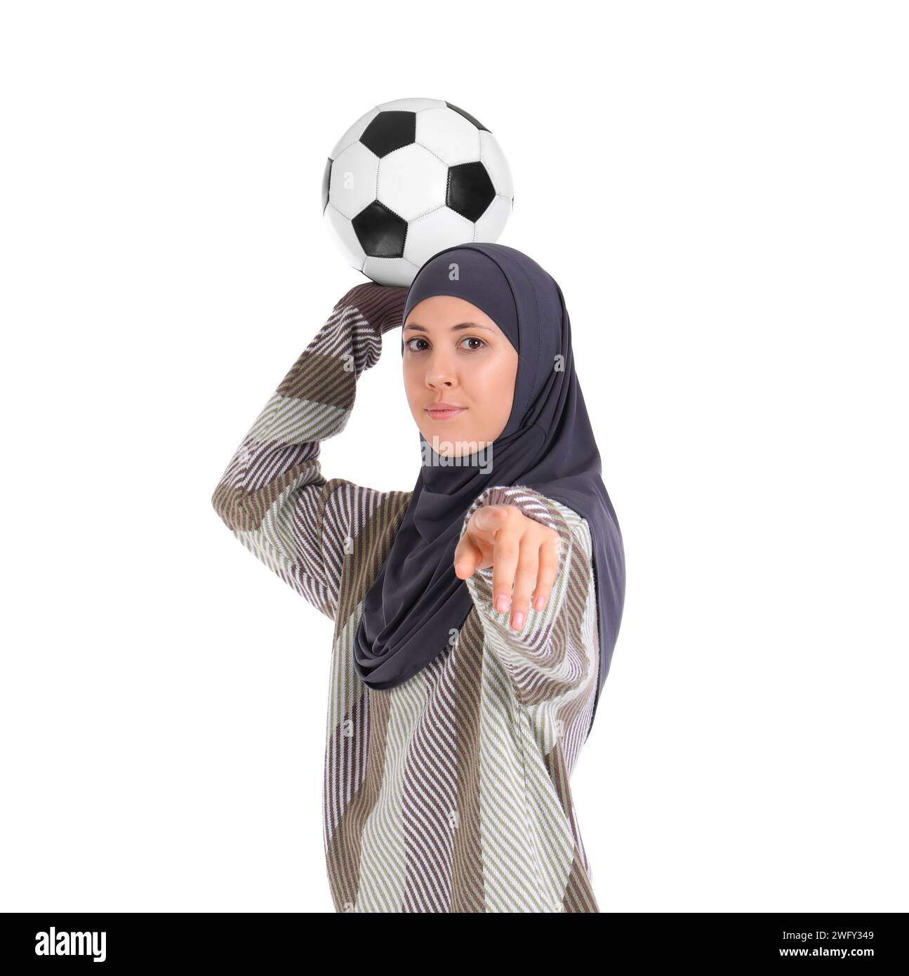 Young beautiful Muslim woman in hijab with soccer ball pointing at viewer on white background Stock Photo