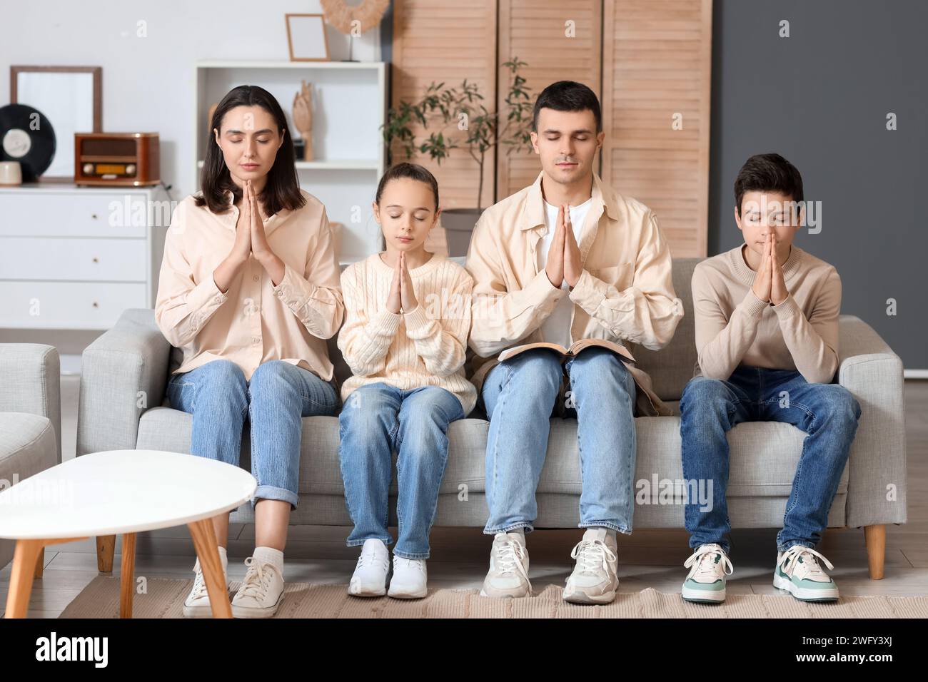 Family with Holy Bible praying on sofa at home Stock Photo