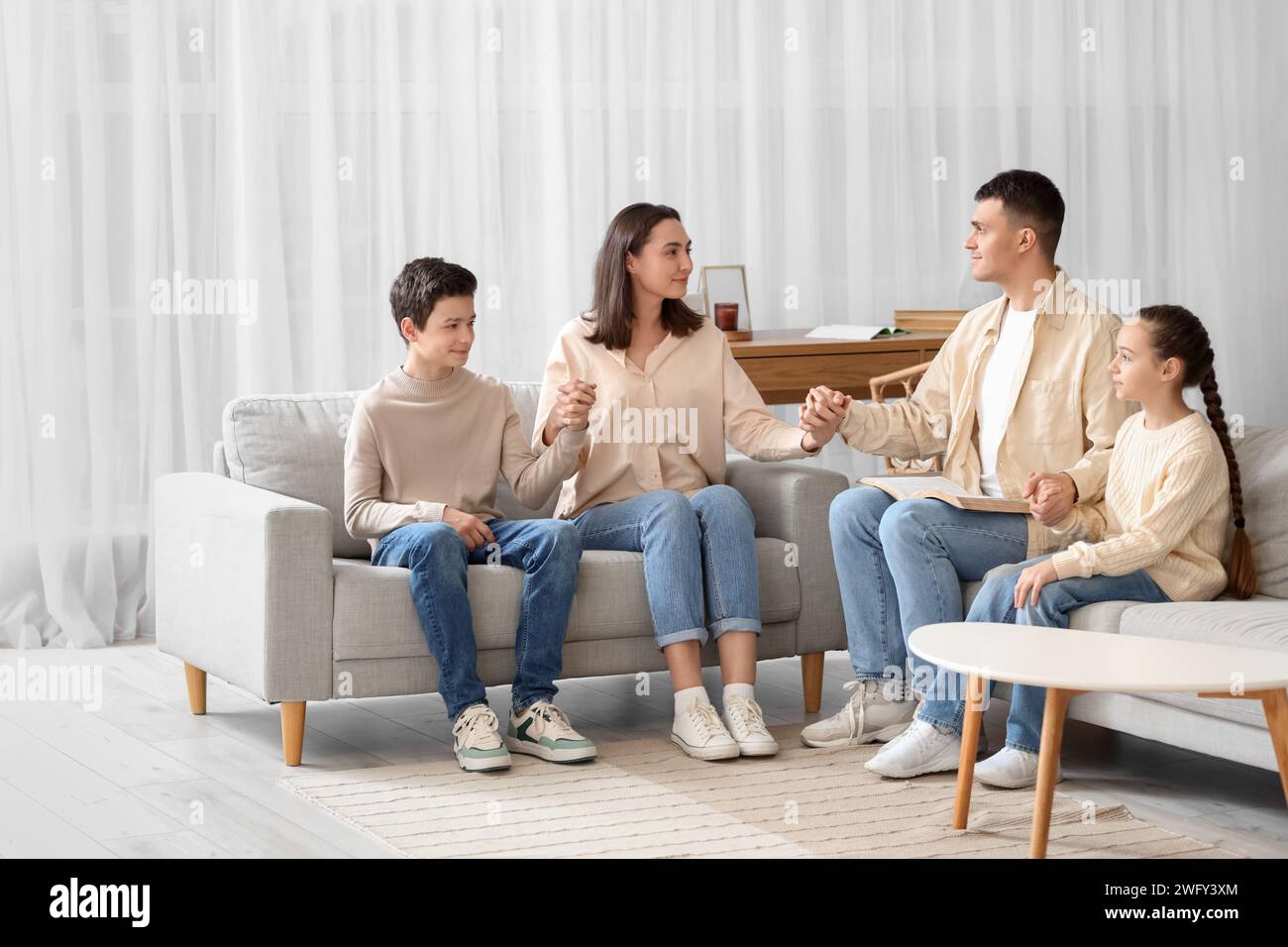 Family with Holy Bible praying on sofa at home Stock Photo