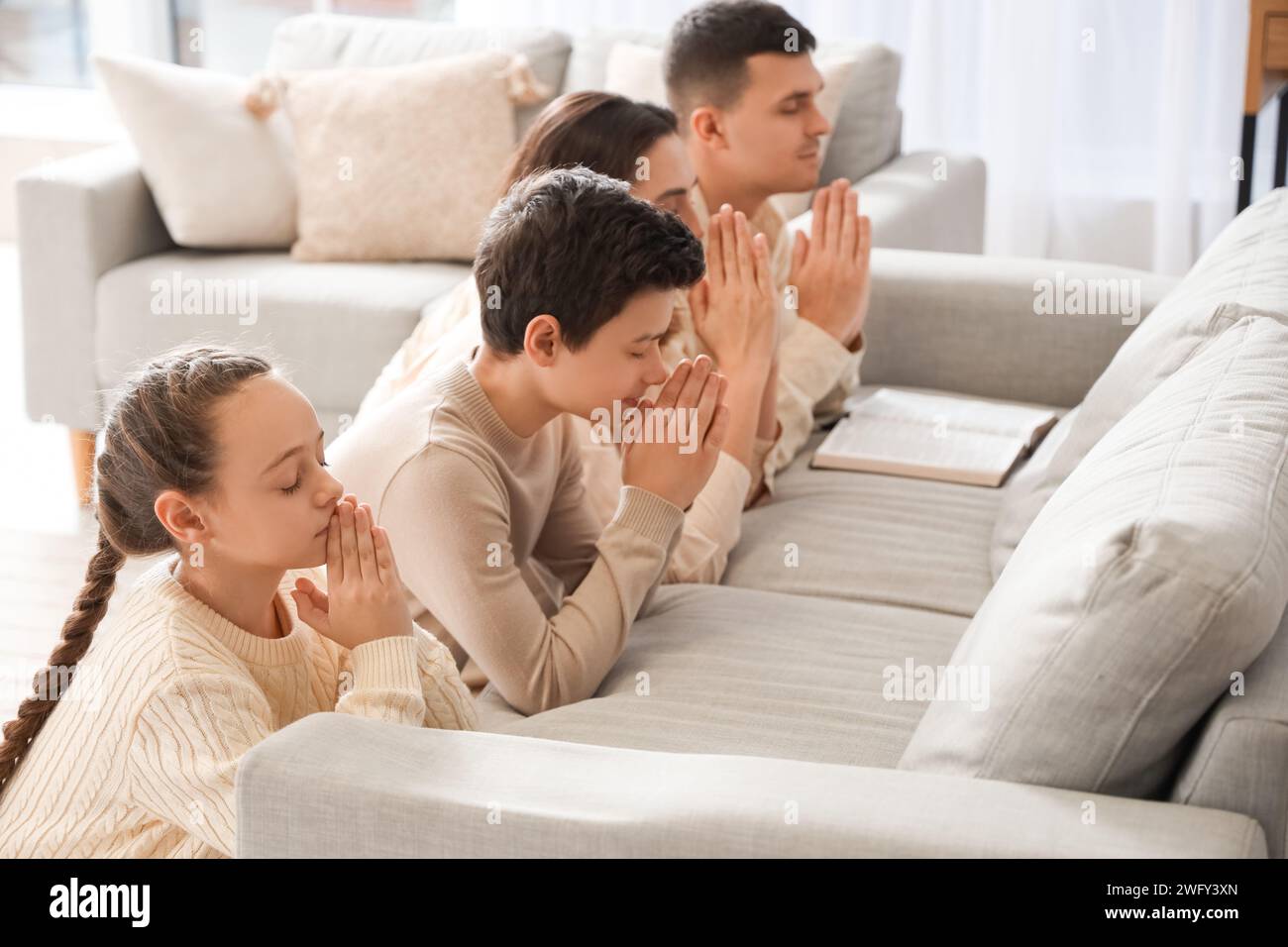 Family with Holy Bible praying behind sofa at home Stock Photo