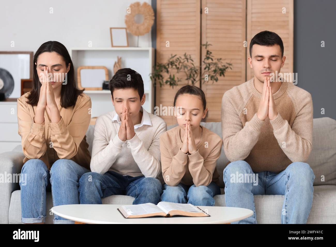 Family praying together on sofa at home Stock Photo