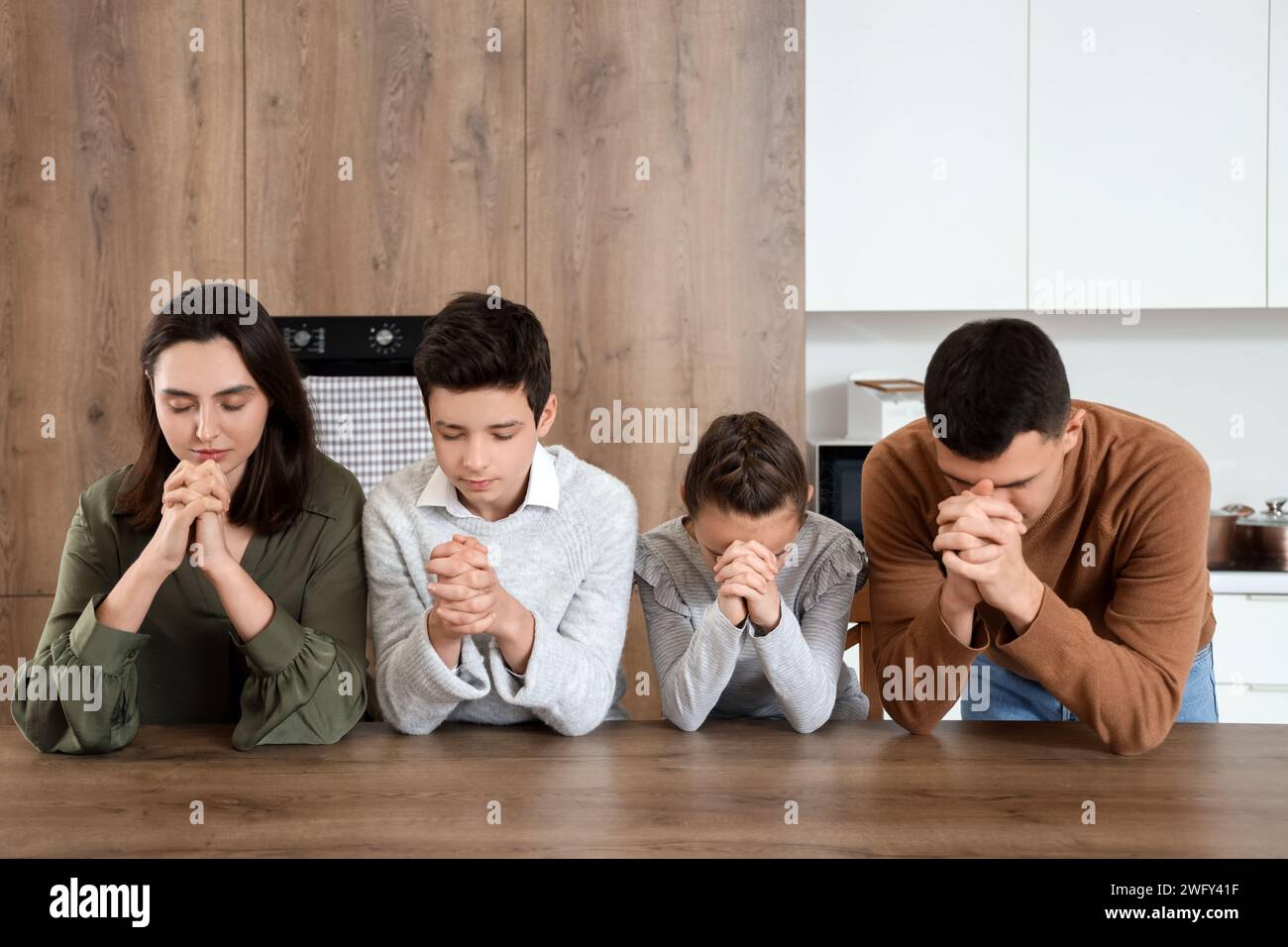 Family praying together at table in kitchen Stock Photo