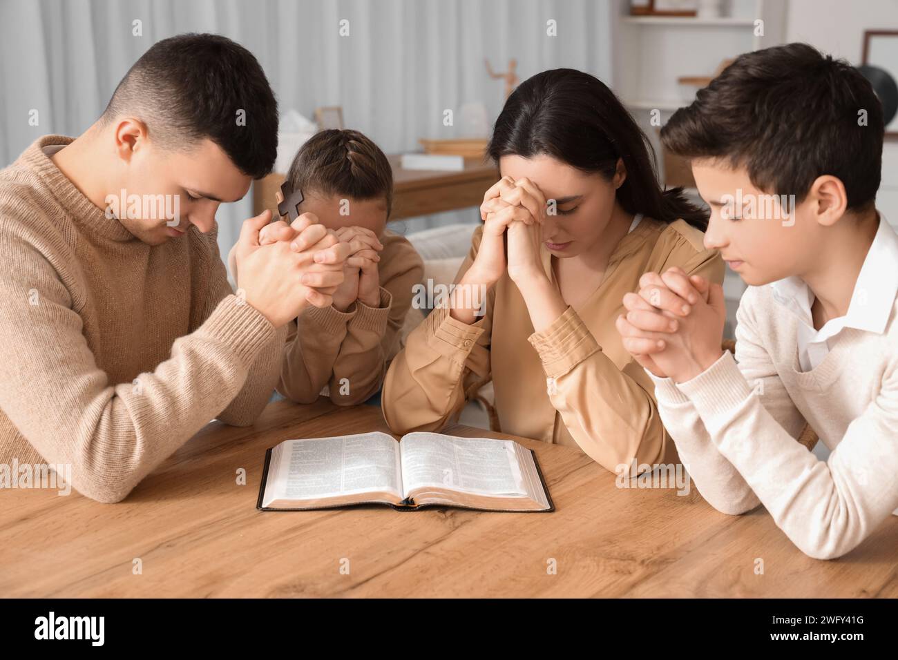 Family praying together with Holy Bible on table at home Stock Photo