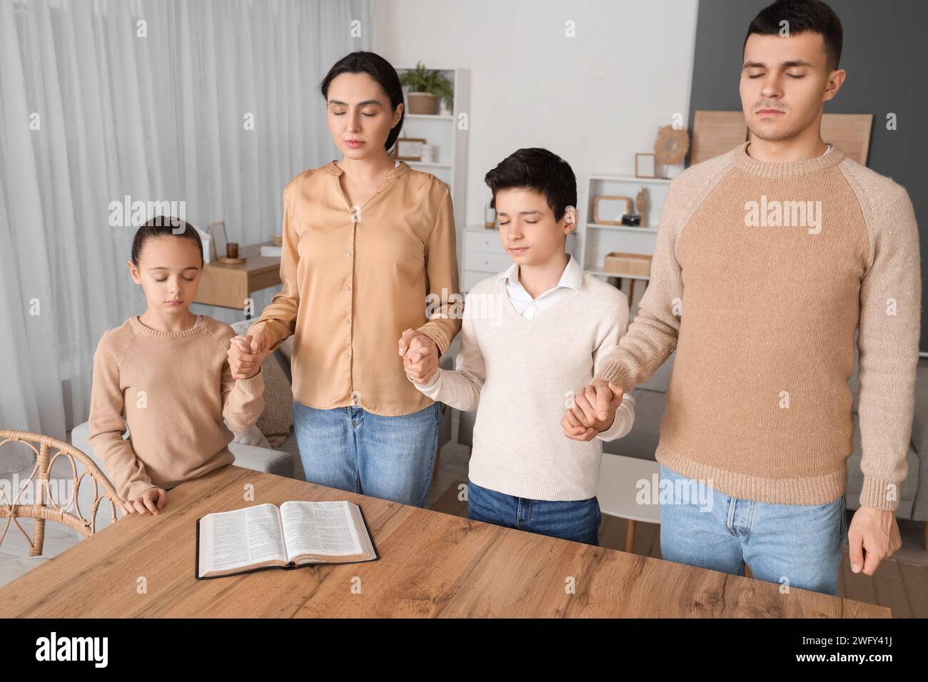 Family praying together with Holy Bible on table at home Stock Photo