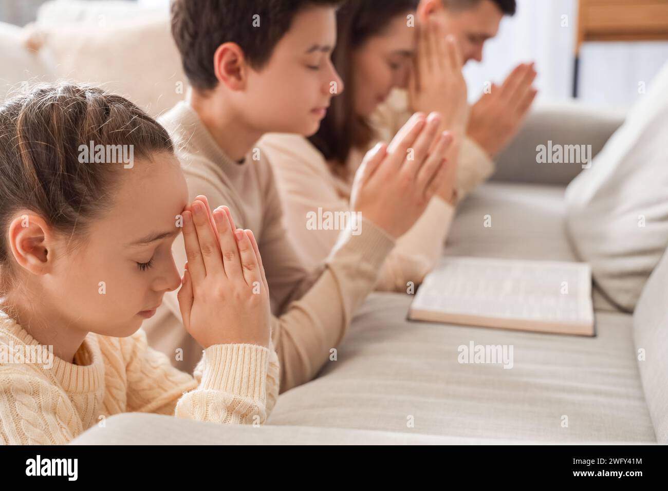 Little girl with her family praying behind sofa at home, closeup Stock Photo