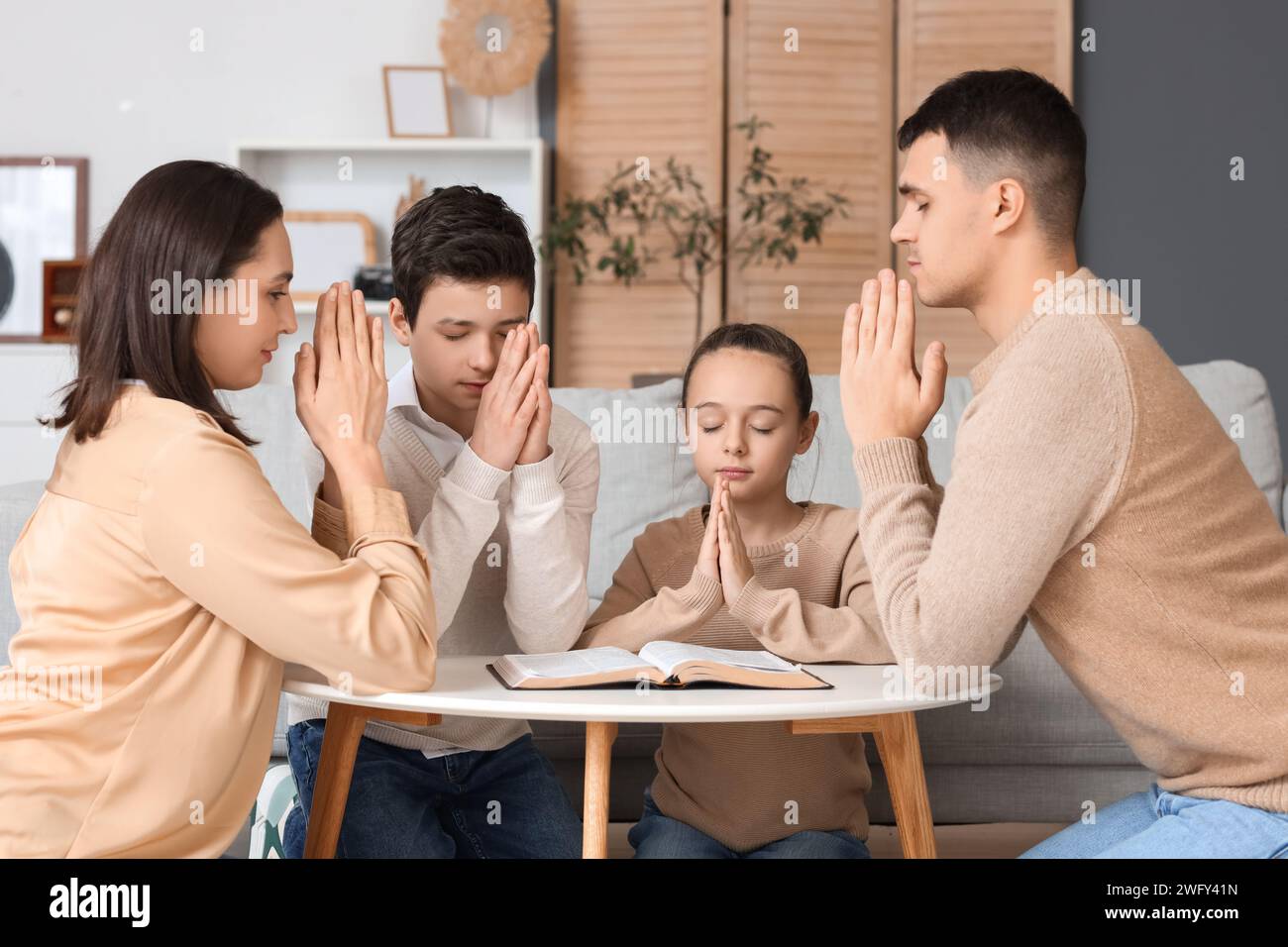 Family praying with Holy Bible on table at home Stock Photo