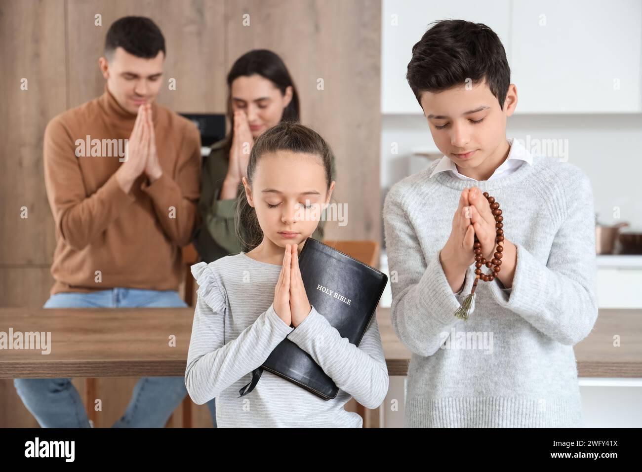 Little children with Holy Bible and beads praying in kitchen Stock Photo