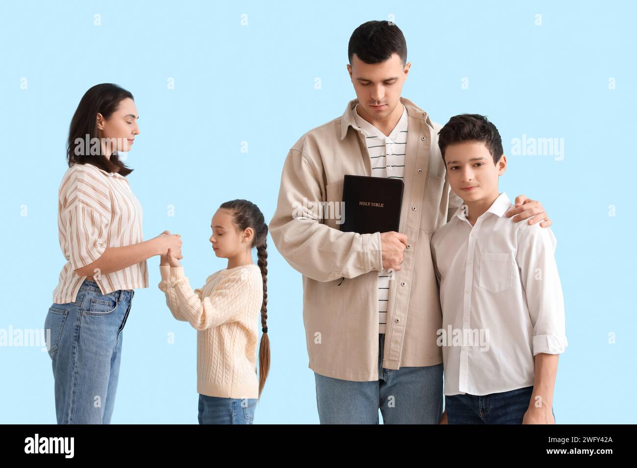 Family with Holy Bible praying together on blue background Stock Photo